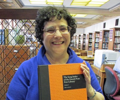 Ellie, holding with pride HER book, in the library she is so proud to work.